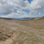 Image of a dusty trail on a sunny day with mountains in the background.