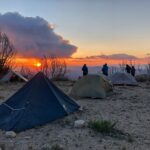 A group of hikers watching the sunset with their tents set up on a mountain.