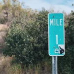 Outdoor scene on a trail with a green sign with 'Mile 1' written on it.